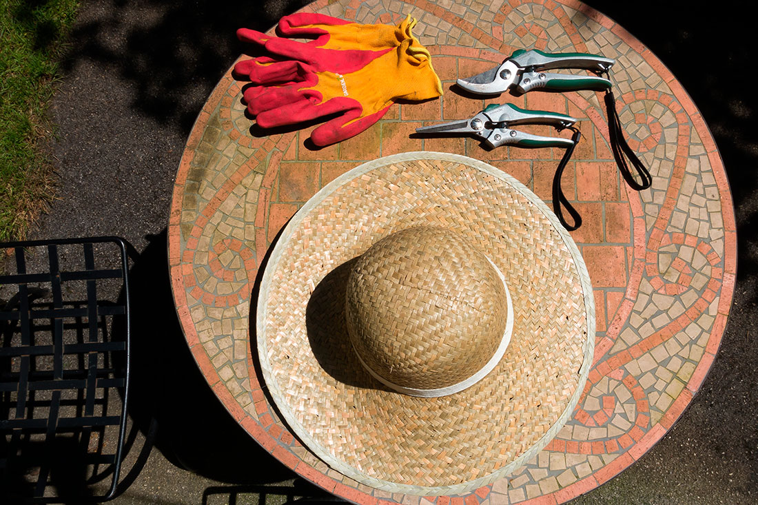 chapeau de paille, gants de jardinage et ciseaux sur une table mosaïque